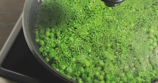 Les pois verts frais sont frits sur une poêle à frire à travers une couverture en verre, Focus sur les gouttes d'eau sur une couverture en verre, un plat lumineux et diététique, un mode de vie sain — Video