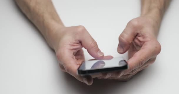 Osoba považuje nové zařízení, ruce drží smartphone na bílém pozadí stolu, prsty stiskněte obrazovku, nové zařízení, tmavá barva — Stock video