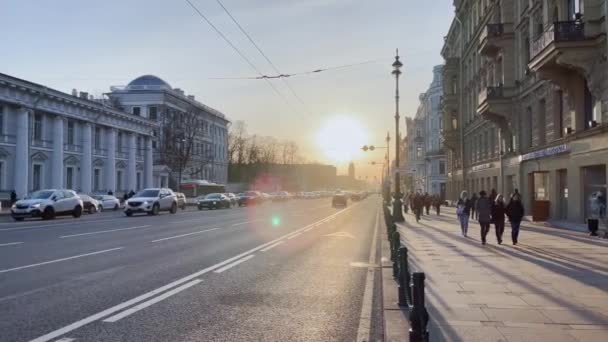 Russland, St.Petersburg, 14. April 2021: Die Architektur des Newski-Prospekts bei Sonnenuntergang im Autoverkehr, das Puppentheater, viele Transportfahrzeuge, lange Schatten von Menschen und Autos — Stockvideo