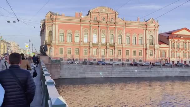 Ryssland, St Petersburg, 14 april 2021: Fasaden av Anichkov Palace och bron, arkitekturen av Nevsky Avenue vid solnedgången, transportfordon, långa skuggor — Stockvideo
