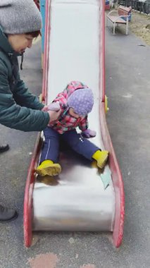 Rusya, St.Petersburg, 11 Nisan 2021: Küçük kız çocuk parkında oynuyor, kız sıcak kıyafetler giyiyor, bulutlu bir hava var, mutlu ve neşeli