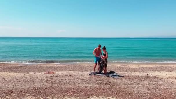 La joven pareja sale de una playa vacía, hermosa chica y chico guapo, se sacude de una puesta de bronceado, sin turistas, agua tranquila azul del mar jónico, un lugar ideal para una privacidad — Vídeo de stock