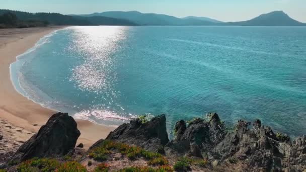 Ένα γραφικό θαλάσσιο τοπίο μιας γαλάζιας λιμνοθάλασσας με μια άδεια δημόσια παραλία την ανατολή του ηλίου, βραχώδη ακτή, βουνά σε φόντο, χωρίς τουρίστες, γαλανά νερά — Αρχείο Βίντεο