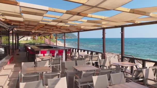 Café vazio sem visitantes em um terraço aberto na costa do Mar Jônico, na Grécia, em um clima claro e ensolarado durante a pandemia Covid-19 — Vídeo de Stock