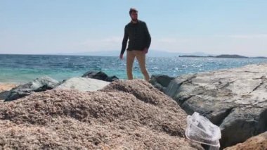 Genç adam güzel bir plajı plastikten temizliyor, gezegenin kirlendiğinden endişe ediyor, ön plandaki kullanılmış plastik kutu.