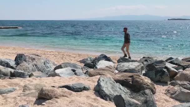 Der junge Mann räumt freiwillig einen schönen Strand von Plastik, er sorgt sich, dass der Planet vermüllt ist, die gebrauchte Plastikbox im Vordergrund — Stockvideo