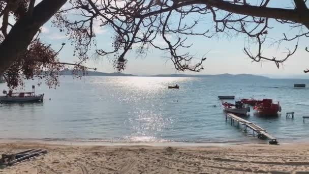 Barco de pesca no caminho do sol no por do sol, Uma paisagem pitoresca do mar de uma lagoa azul com uma praia pública vazia através de banco de árvore no nascer do sol, montanhas em um fundo, sem turistas, água azul — Vídeo de Stock