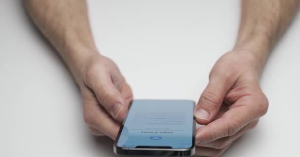 Россия, Санкт-Петербург, 09 апреля 2021 года: человек рассматривает новое устройство, руки держат смартфон на белом фоне стола, пальцы нажимают на экран, новое устройство, темный цвет — стоковое видео