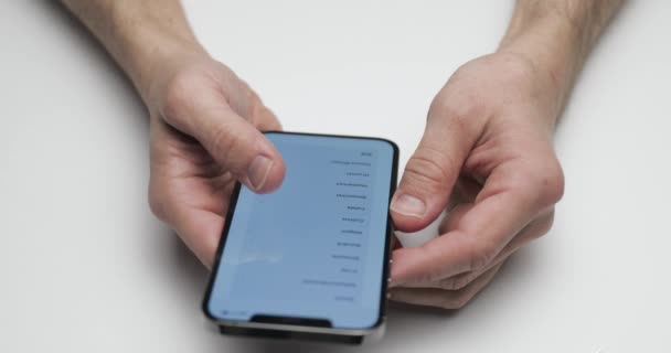 Russia, St Petersburg, 09 April 2021: The person setups the new device, hands are holding the smartphone on white table background, fingers press the screen, dark color — Stock Video