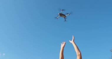 Güneşli bir havada mavi gökyüzüne karşı hareket etmeden uçan bir dronun alt görüntüsü, eller bir drona, sensörlere ve kameraya uzanır, hareket halinde bıçaklar, yakın çekim görüntüleri.