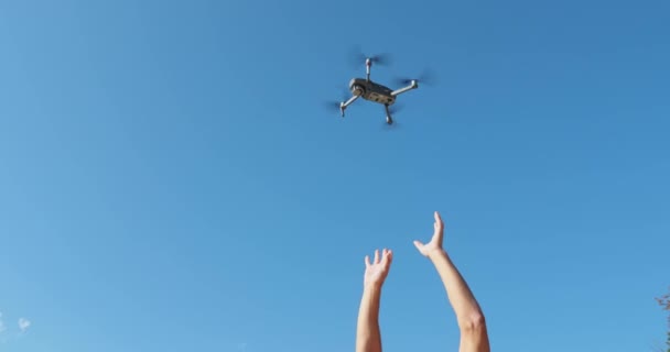 Vista inferior de um drone voador sem movimento contra um céu azul em tempo ensolarado, Mãos alcançam um drone, sensores e uma câmera, lâminas em movimento, imagens de close-up — Vídeo de Stock