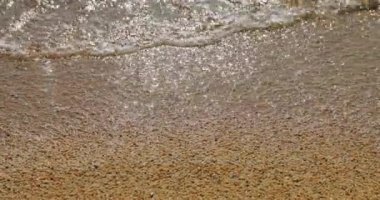 Çakıl kumsalının, kaba kumların, kumların, kumların üzerinde dalgaların, güneşin altında ışıldayan ıslak taşların, suyun üzerinde yansıyan güneşin yakın çekim görüntüleri.