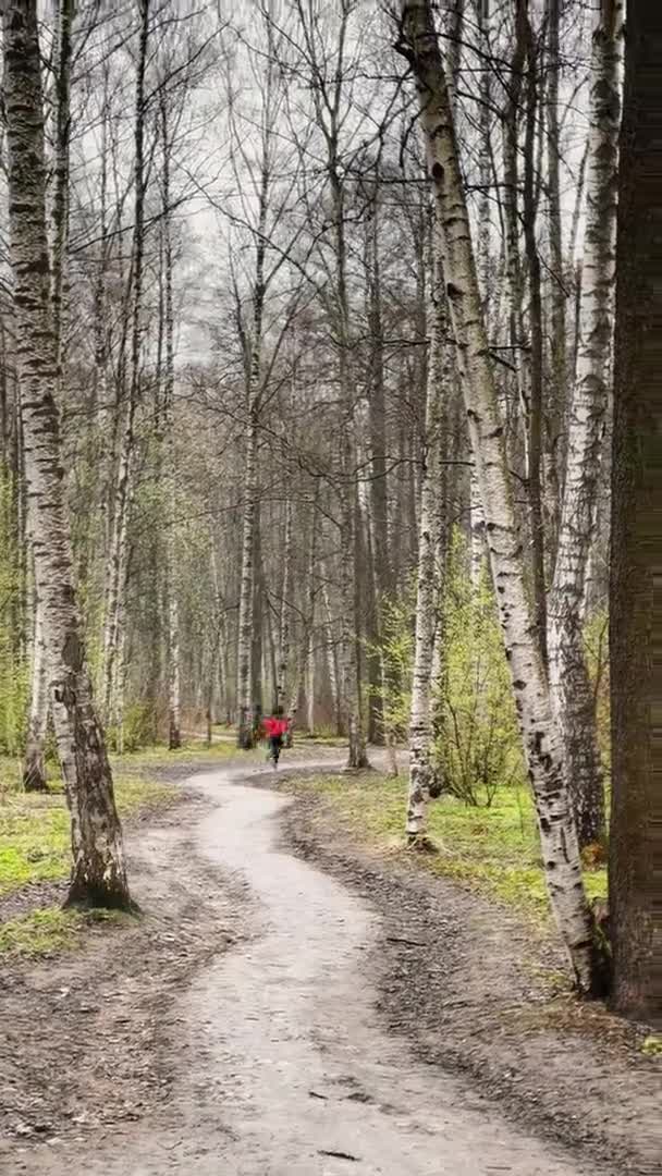 Os jovens estão correndo, ele vestiu-se com jaqueta de chuva vermelha e snickers, esportes ao ar livre, as imagens verticais do parque da primavera no dia nublado, está nevando, primeira grama verde — Vídeo de Stock