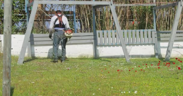 Grecia, Calcidica, 15 aprile 2019: L'operaio in tuta taglia un'erba verde con un tosaerba a benzina su un prato con un tempo soleggiato — Video Stock