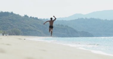 Yüzme şortu içinde harika bir vücudu olan yakışıklı bir adam sabahın köründe ıssız bir plajda eğleniyor, bir şampiyon gibi zıplıyor, hızla sahilde koşuyor, vücudunu gösteriyor ve poz veriyor.