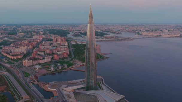 Ryssland, St Petersburg, 16 maj 2021: Drönare av att flyga bort från den högsta skyskrapan i Europa Lakhta Center vid rosa solnedgång, högkvarter för oljebolaget Gazprom, stadion Gazprom Arena på bakgrunden — Stockvideo