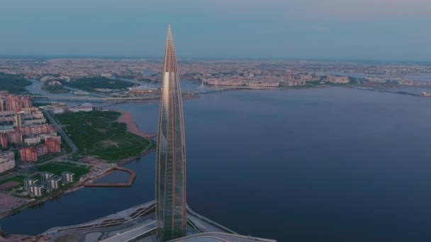 Ryssland, St Petersburg, 16 maj 2021: Drönare av att flyga bort från den högsta skyskrapan i Europa Lakhta Center vid rosa solnedgång, högkvarter för oljebolaget Gazprom, stadion Gazprom Arena på bakgrunden — Stockvideo