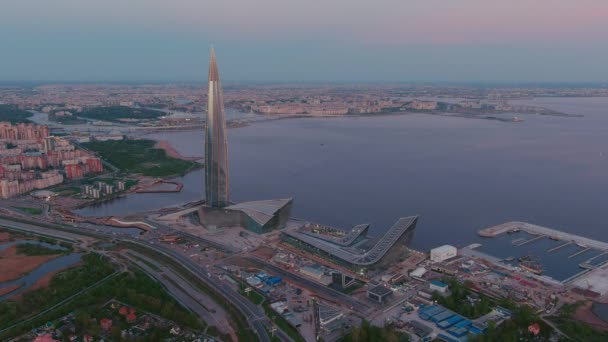 Ryssland, St Petersburg, 16 maj 2021: Drönare av att flyga bort från den högsta skyskrapan i Europa Lakhta Center vid rosa solnedgång, högkvarter för oljebolaget Gazprom, stadion Gazprom Arena på bakgrunden — Stockvideo