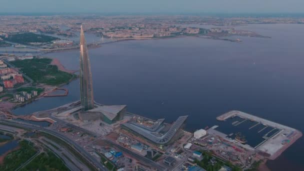 Rússia, São Petersburgo, 16 de maio de 2021: Drone de voar para longe do arranha-céu mais alto da Europa Lakhta Center ao pôr-do-sol rosa, sede da empresa petrolífera Gazprom, estádio Gazprom Arena em segundo plano — Vídeo de Stock