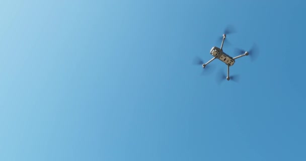 Вид знизу літаючого безпілотника без руху до блакитного неба в сонячну погоду, руки досягають безпілотника, датчиків і камери, лопаті в русі, крупним планом кадри — стокове відео