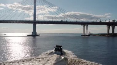 Rusya, St. Petersburg, 01 Eylül 2020: Gençler açık güneşli bir havada teknenin arkasında sörf tahtasına biniyor, Gazprom arenası ve kablo destekli bir köprü arka planda. 