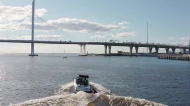 Rusya, St. Petersburg, 01 Eylül 2020: Gençler açık güneşli bir havada teknenin arkasında sörf tahtasına biniyor, Gazprom arenası ve kablo destekli bir köprü arka planda. 