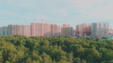 İnsansız hava aracı güneş batarken inşaat halindeki büyük konutlara doğru uçuyor, inşaat vinçleri, yeşil ağaçlar, St. Petersburg, Rusya