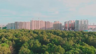 İnsansız hava aracı güneş batarken inşaat halindeki büyük konutlara doğru uçuyor, inşaat vinçleri, yeşil ağaçlar, St. Petersburg, Rusya