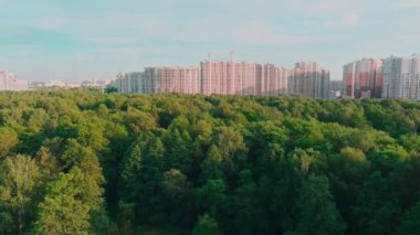 İnsansız hava aracı güneş batarken inşaat halindeki büyük konutlara doğru uçuyor, inşaat vinçleri, yeşil ağaçlar, St. Petersburg, Rusya