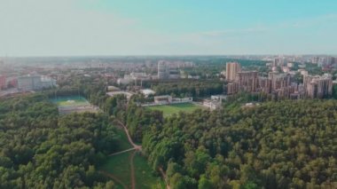 İnsansız hava aracı gün batımında inşaat halindeki büyük konutlara doğru uçuyor. İnşaat vinçleri, yeşil ağaçlar, St. Petersburg, Rusya, futbol stadyumu.