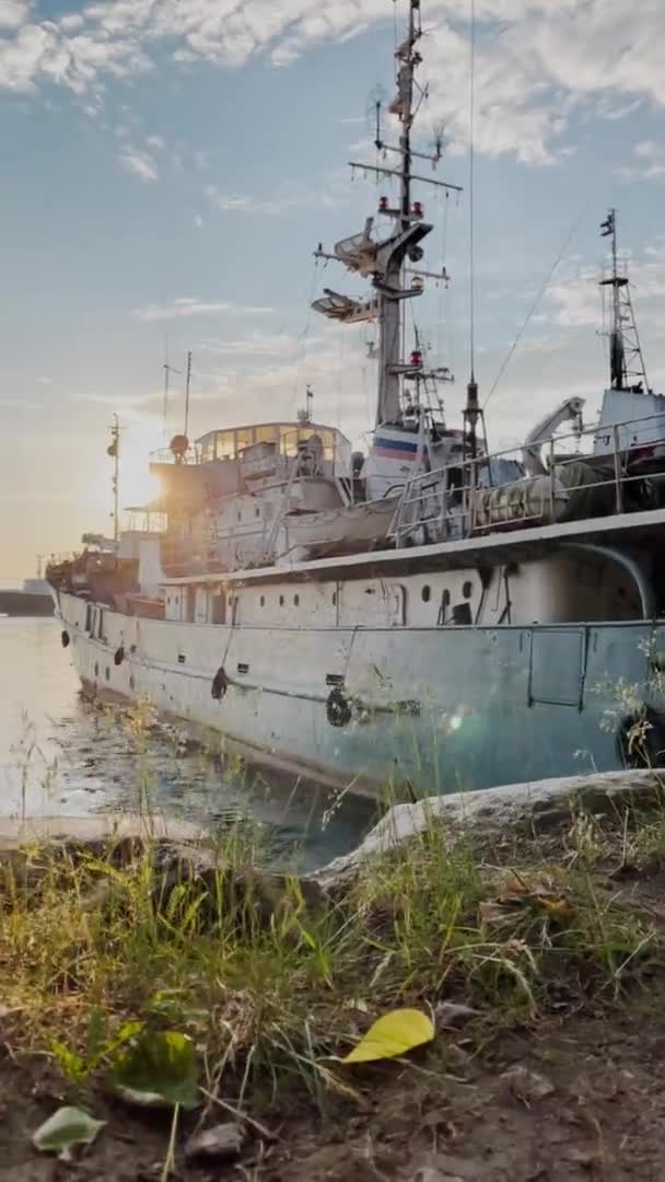 Vídeo vertical del viejo buque pesquero parado en la costa a través de una hierba al amanecer, camino del sol, puerto con muchos barcos viejos, reflejos del sol, silencio y tranquilidad — Vídeos de Stock
