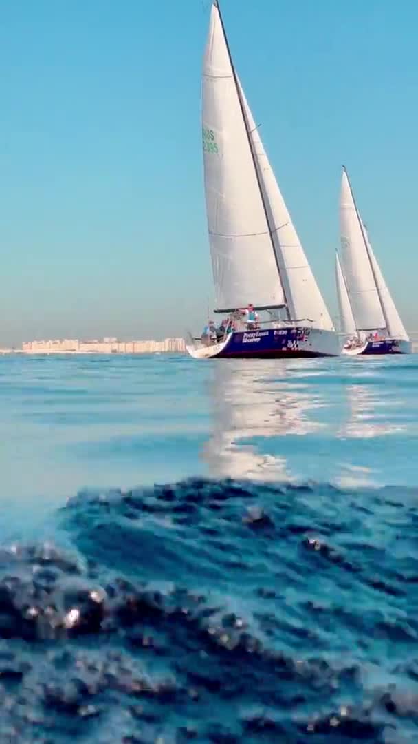 Russia, St.Petersburg, 18 June 2021: Some sailboats in a list goes by sea, Splashes water in the foreground, the clear sky, regatta, reflection of sail on the water, Foamy path from the boat — Stock Video