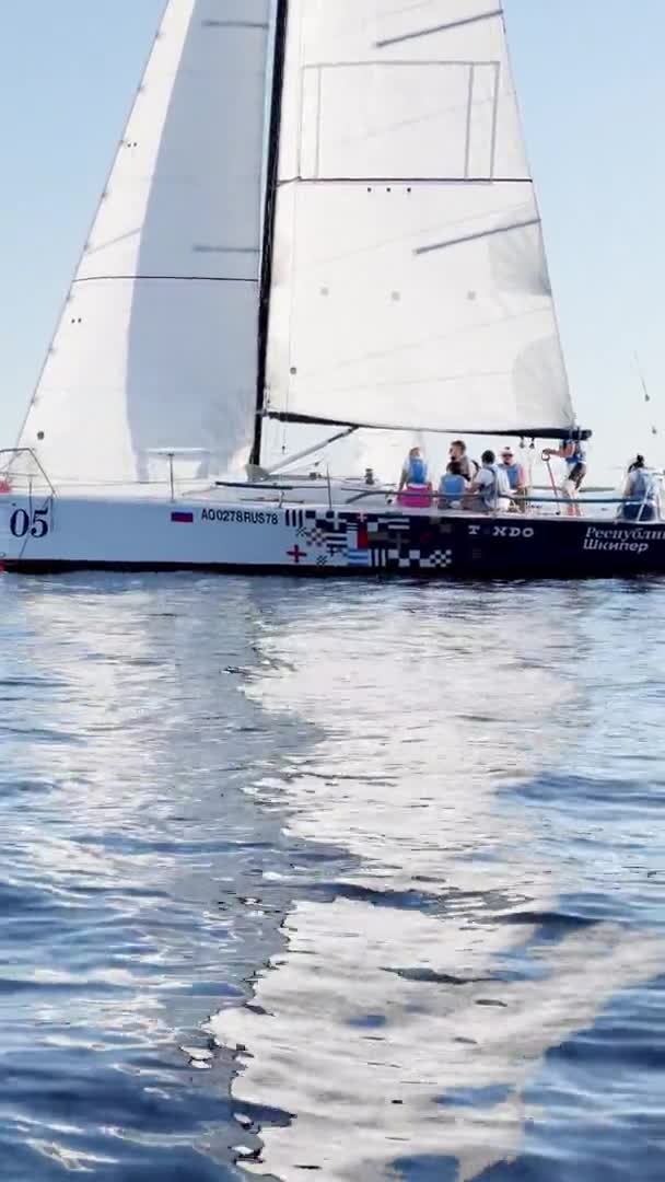 Russia, St.Petersburg, 18 June 2021: Participants of a sail regatta are dressed in life jackets, still water, the clear sky, reflection of sail on the water, small waves — Stock Video