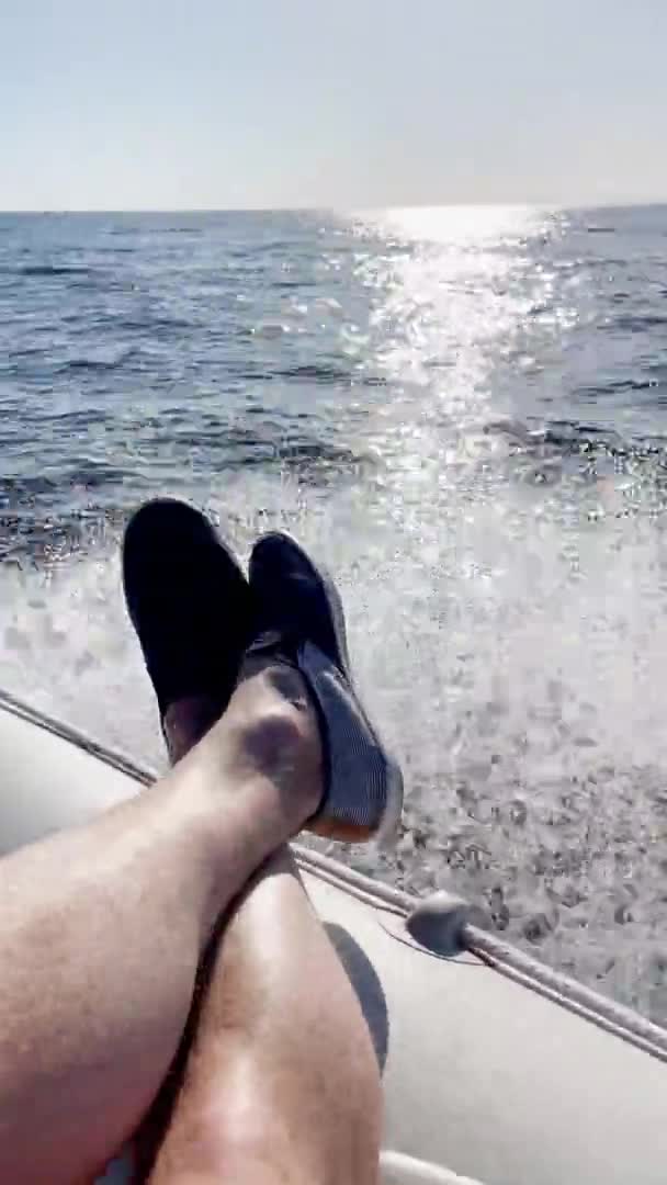 Erkeklerin ayakları rahat ayakkabılar giyer botun kenarına uzanır, tekne açık ve güneşli bir havada hızla yüzer, teknenin altından su sıçrar. — Stok video