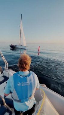 Rusya, St.Petersburg, 18 Haziran 2021: Bir yelkenli yarışının hakimi yargı teknesinin yarışını izler, yelkenli yarışına katılanlar can yelekleri giyer, denizde yelkenin yansıması, güneşlidir