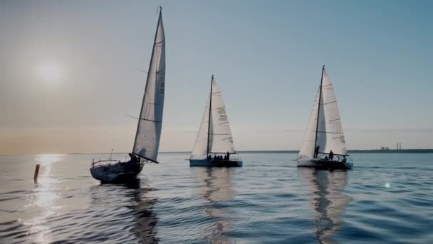 Russie, Saint-Pétersbourg, 18 Juin 2021 : Quelques voiliers dans une liste va par la mer au coucher du soleil, eau calme, le ciel clair, régate de voile, réflexion de la voile sur l'eau, petites vagues — Video