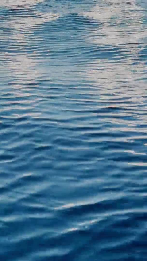 Вертикальные кадры отражения паруса белого цвета на воде, небольшие волны, синяя вода в движении — стоковое видео