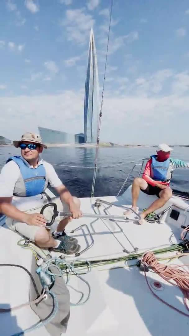 Rusia, San Petersburgo, 20 de junio de 2021: Regata de veleros en el día soleado, barcos corren diferente viraje, equipo en el barco, el cielo despejado, vela, reflejo de la vela en el agua, rascacielos centro de Lakhta — Vídeo de stock