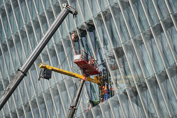 Russland, St. Petersburg, 23. Juli 2021: Hochhausbau für den Ölkonzern Gazprom, eine Fassadenverglasung, Bauarbeiter heben mit dem Hochbaukran große Gläser in die Höhe — Stockfoto