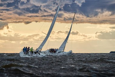 Rusya, St. Petersburg, 23 Temmuz 2021: Gün batımında ufukta iki yelkenlinin yarışması, farklı renklerde inanılmaz fırtına gökyüzü, yarış, büyük dalgalar, yelkenli yarışı, bulutlu hava, güneş ışınları