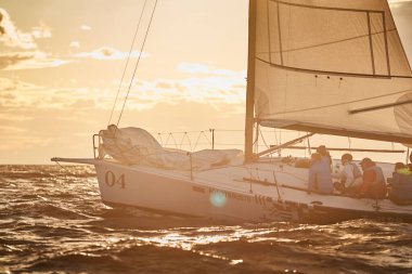 Rusya, St. Petersburg, 23 Temmuz 2021: Gün batımında denizde yelkenli yarışı, farklı renklerde inanılmaz fırtına gökyüzü, yarış, büyük dalgalar, yelkenli yarışı, güneş ışınları, takım çalışması