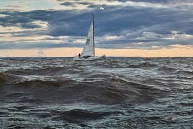 Rusya, St. Petersburg, 23 Temmuz 2021: Gün batımında denizde yelkenli yarışı, farklı renklerde inanılmaz fırtına gökyüzü, yarış, büyük dalgalar, yelkenli yarışı, güneş ışınları, takım çalışması