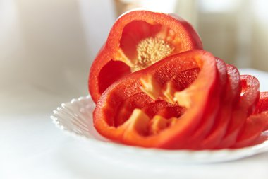 Beyaz bir arka planda ele beyaz tabakta kırmızı dolmalık biber yatıyor