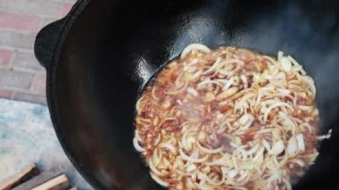 Ateşte büyük bir dökme demir kazanda Özbek milli çanak pilav, altın kahverengi, kuzu, havuç, koyun yağı, yağ kuyruk, susam yağı, sarımsak kadar doğranmış soğan kızartma