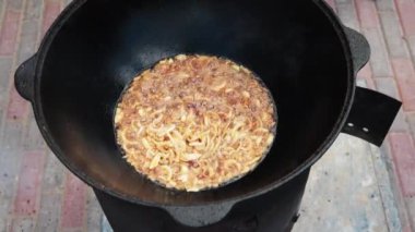 Ateşte büyük bir dökme demir kazanda Özbek milli çanak pilav, altın kahverengi, kuzu, havuç, koyun yağı, yağ kuyruk, susam yağı, sarımsak kadar doğranmış soğan kızartma