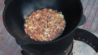 Ateşte büyük bir dökme demir kazanda Özbek milli çanak pilav, altın kahverengi, kuzu, havuç, koyun yağı, yağ kuyruk, susam yağı, sarımsak kadar doğranmış soğan kızartma