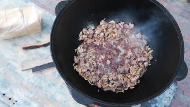 Usbekisches Nationalgericht pilaf in einem großen gusseisernen Kessel auf dem Feuer, fügen Sie die Lammstücke hinzu und rühren Braten, Reis, Karotten, Hammelfett, den fetten Schwanz, Sesamöl, Zwiebeln, Knoblauch, rote Chilischote — Stockvideo