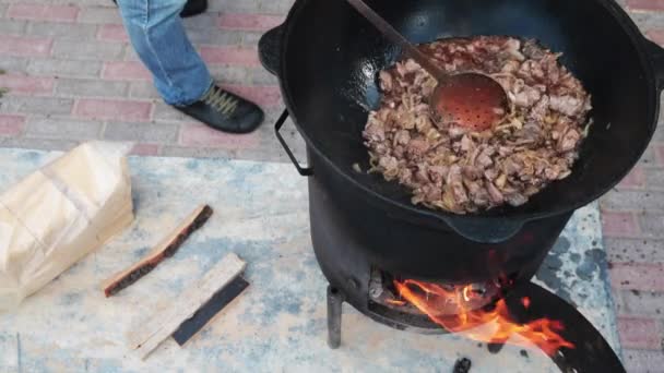 Usbekisches Nationalgericht pilaf in einem großen gusseisernen Kessel auf dem Feuer, fügen Sie die Lammstücke hinzu und rühren Braten, Reis, Karotten, Hammelfett, den fetten Schwanz, Sesamöl, Zwiebeln, Knoblauch, rote Chilischote — Stockvideo