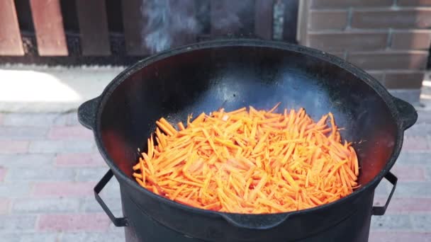 Oezbeekse nationale gerecht Pilaf in een grote gietijzeren ketel op het vuur, voeg gesneden rode wortelen, rijst, lam, schapenvlees vet, de dikke staart, sesamolie, ui, knoflook, rode hete Chili peper — Stockvideo