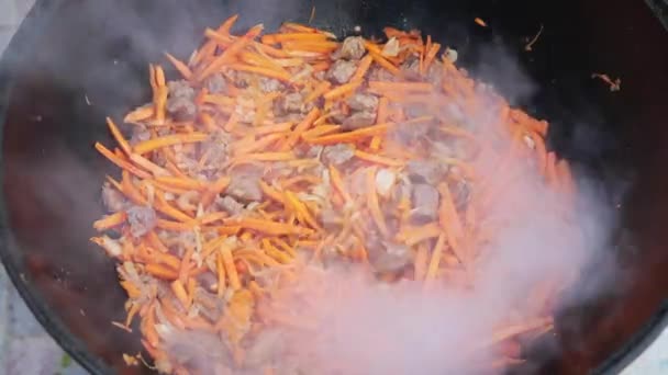 火の上に大きな鋳鉄大鍋にウズベキスタンの国民料理ピラフ、スライスされた赤ニンジン、米、ラム、羊肉、脂肪の尾、ゴマ油、玉ねぎ、ニンニク、赤唐辛子を追加 — ストック動画